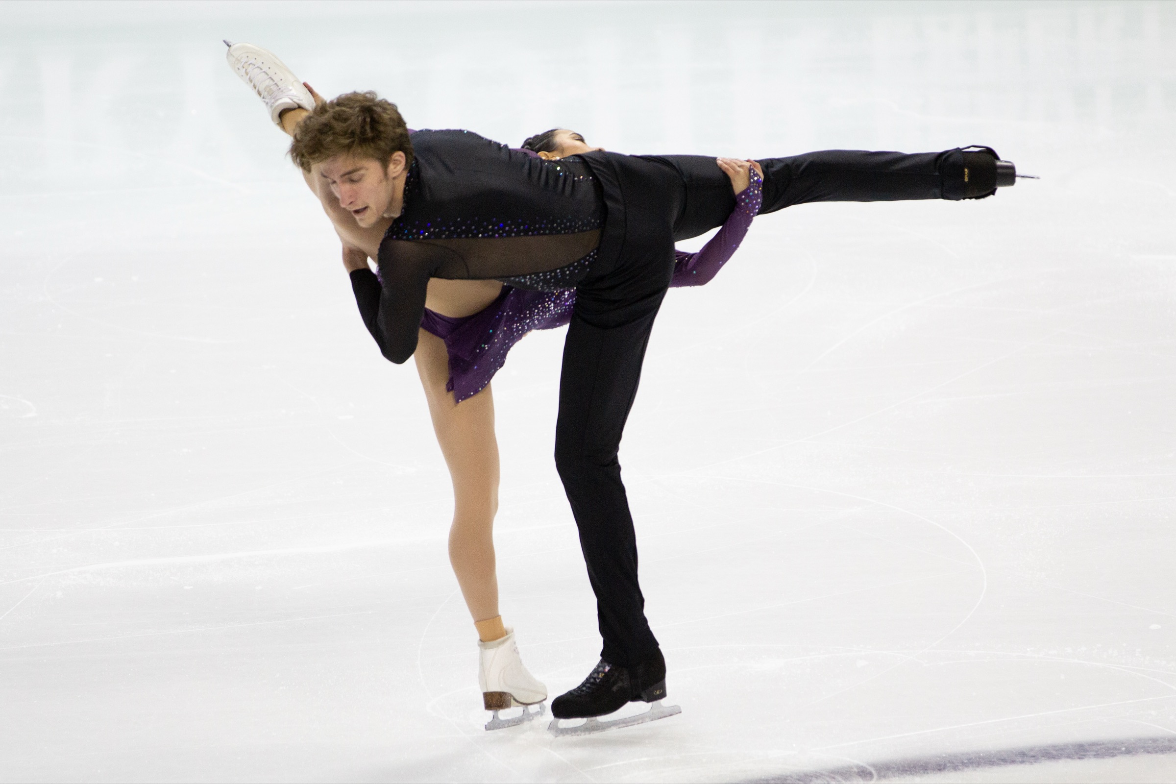 A figure skating pair mid-lift on the ice during a competition free skate, arms extended, captured in dramatic motion.