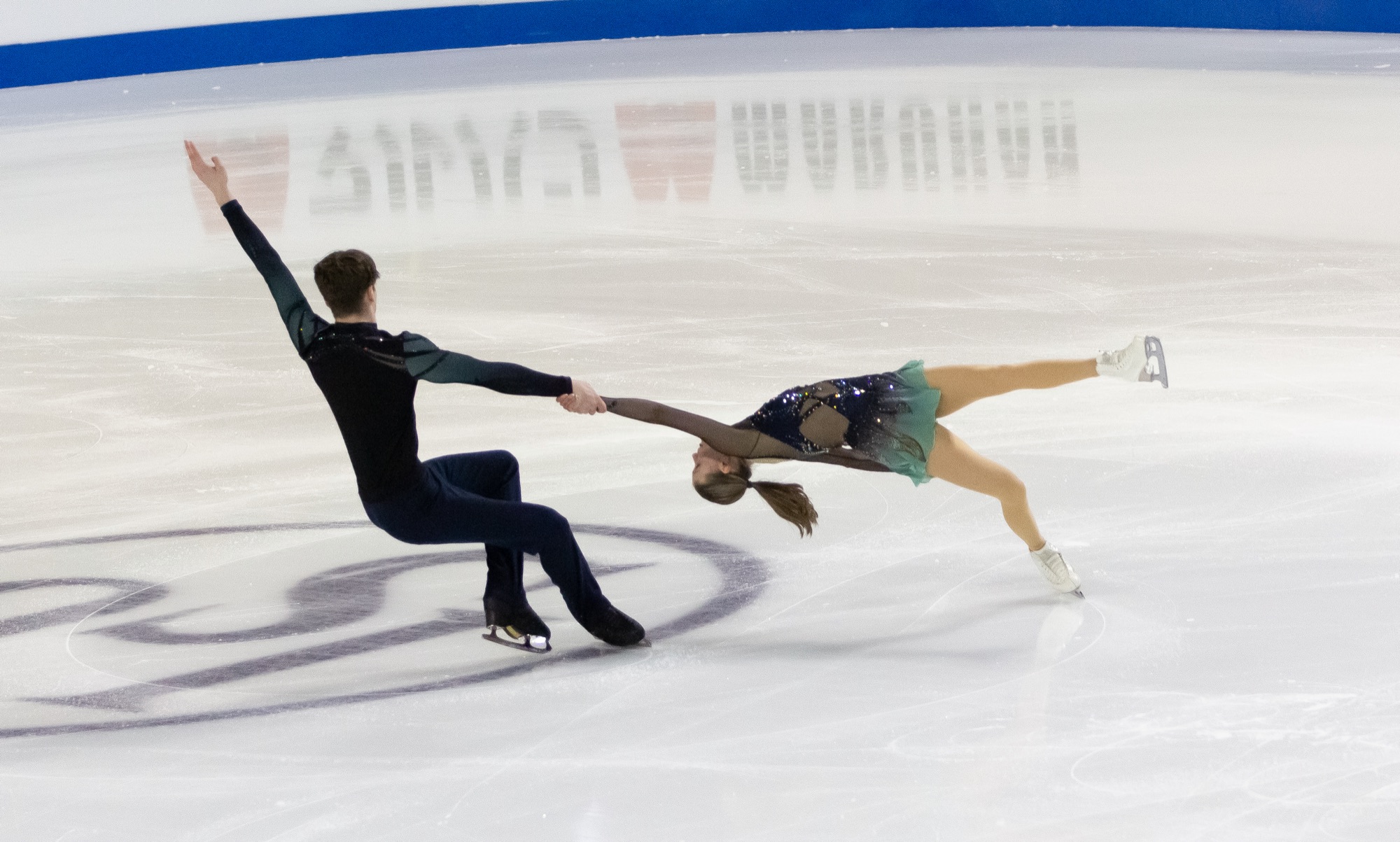 A figure skating pair performing a free skate element on the ice at a competition, in full motion.